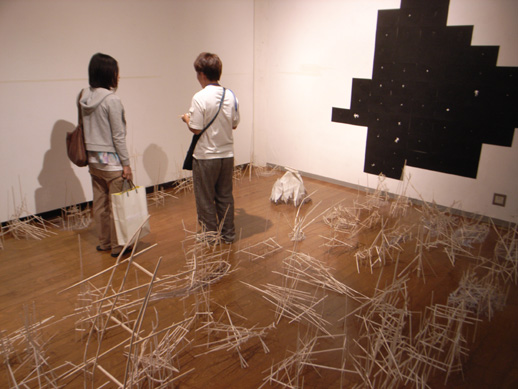Tomoko Iwata (right) standing in her installation work, talking about it to a guest.