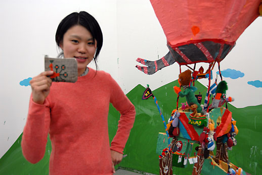 Misaki Kawai standing next to her installation work hanging from the ceiling.