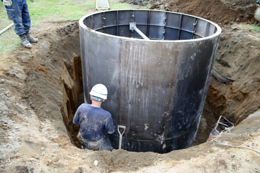 円形の穴が崩れないように、スムーズの面が外向きの型枠が地中に入れられ、建設会社の土工が周りの地面を締め固めます