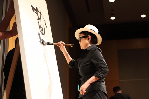 Yoko Ono writes calligraphy of hope onto a canvas, to be copied and sold for charity by Mori Art Museum.