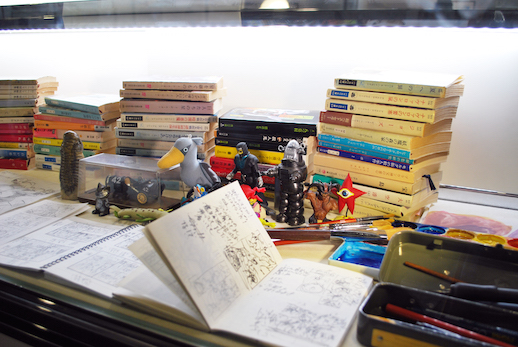 Sketchbooks, books, and figurines from the artist's personal collection, including Robby the robot from 'Forbidden Planet' and Go Nagai's 'Devilman.'