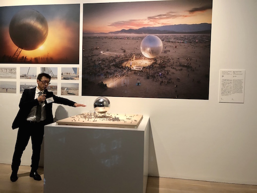 Future and the Arts curator Kenichi Kondo speaks in front of a display for 'The Orb' by Bjarke Ingels and Jakob Lange