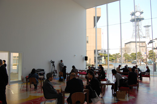 休憩スペースの内部。床には十和田市の伝統工芸である南部裂織をモチーフにしたマイケル・リンの作品。全体的に館内からは外部の都市空間を、外部の都市空間からは美術館の内部の様子を感じとることができる開放的なつくりが特徴。
