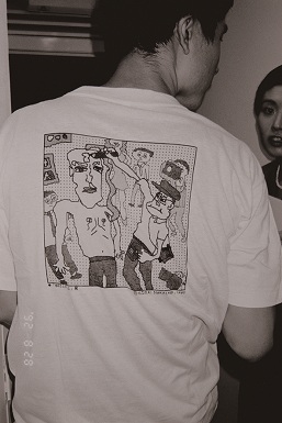 「中村と村上」ソウル展でパフォーマンスする池宮中夫にジゾイングする小沢剛を描いたイラストTシャツを着る中ザワヒデキ氏