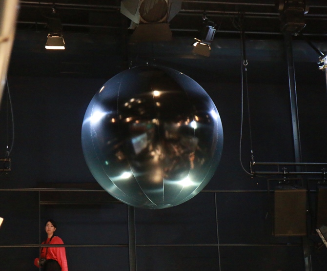 天井にはミラーボールではなく……黒い球体。日本最大のスペクタクルといもいえる大阪万博開会式の「司祭」のようであった岡本太郎作、太陽の塔の「黒い太陽」を表象している